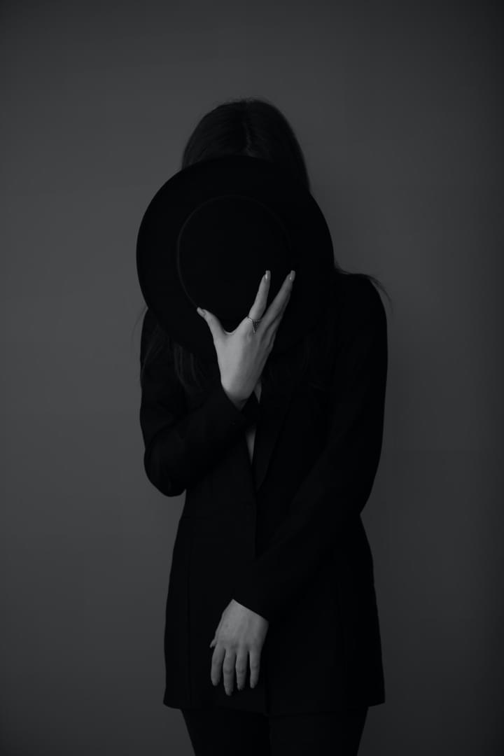 A woman in black hides her face with a hat